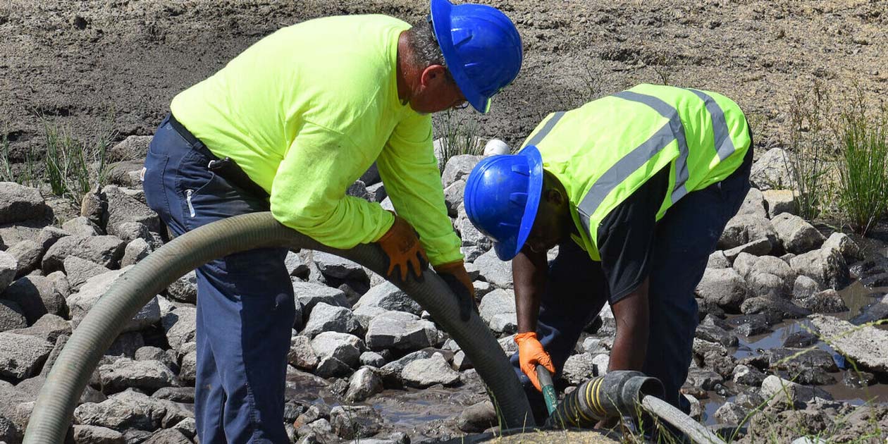 Two wastewater technicians working together to direct water and hoses into a storm water drain system