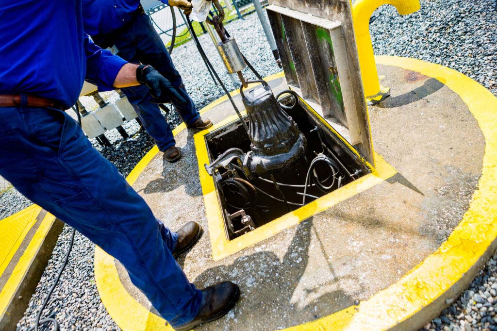 Two wastewater operators service an underground water pump through the hatch of a utility vault